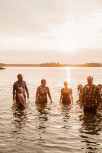En liten grupp människor som står i vattnet under en solnedgång.