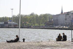 På bilden syns Södra kajen i Helsingfors. Två personersitter på kajen och en lutar sig mot en lyktstolpe.