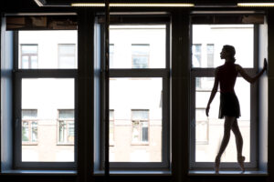 Ett stort fönster fotograferat i motljus. Längst till höger syns ballerinan Anna Palomäki i profil.