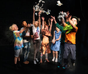 Barn i teaterskolan Konfetti, fotograferade mot svart bakgrund, kastande konfetti rakt upp i luften.