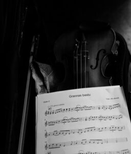 På bilderna syns ett notblad med titeln "Grannas bastu" för tredje violin. I bakgrunden syns en violin och en stråke.