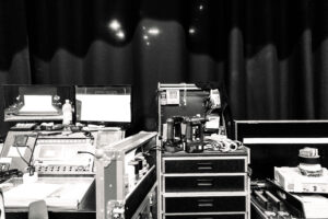 En svartvit bild tagen backstage på Helsingfors stadsteater. Vi ser ett mixerbord, flertalet lådor, borrmaskiner och annat som kan behövas före en show.
