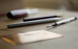På ett träbord ligger pennor av olika slag och en skiss på ett gulnat papper,