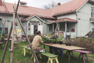 Tre personer sitter på bänkar runt ett bord i en trädgård. Huset i bakgrunden är Lilla Villan i Sibbo.