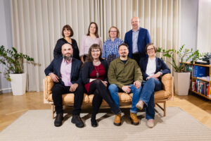 Kulturfondens åtta ombudsmän sitter i en soffa eller står bakom ryggstödet. Alla tittar in i kameran och ser glada ut.
