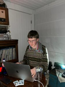 En ung kille i stickad tröja sitter framför en dator.